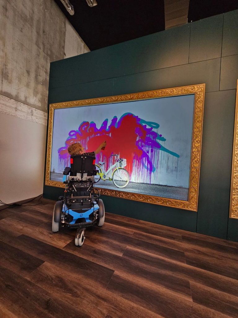 Enfant en fauteuil roulant qui graffe sur le mur Digital Graffiti, une activité accessible à tous