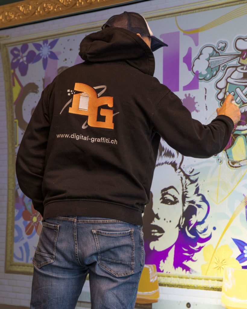 L'artiste Kesh, sweat Digital Graffiti, devant un mur